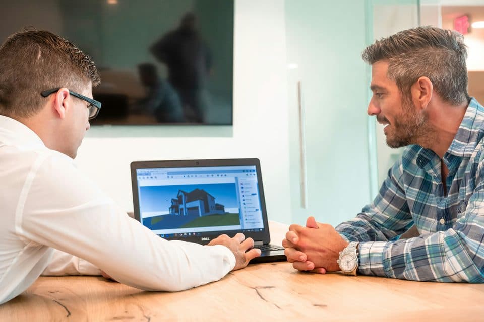 An agent showing a client a 3D model of a house on a laptop